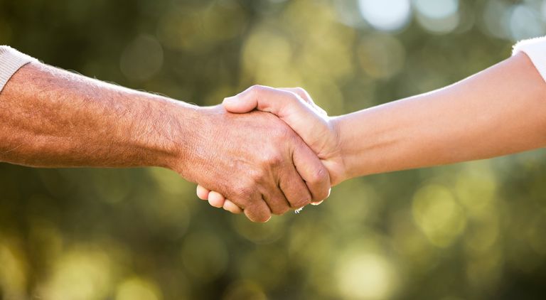 Två händer i ett handslag med en grönskande bakgrund