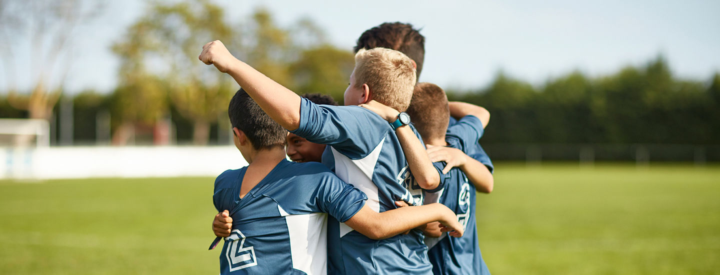 Barn iklädda blå matchkläder på en fotbollsplan slår armarna om varandra för att fira