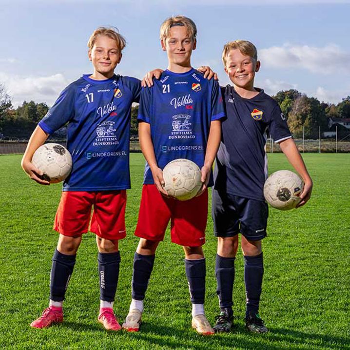Tre pojkar som ler på en fotbollsplan