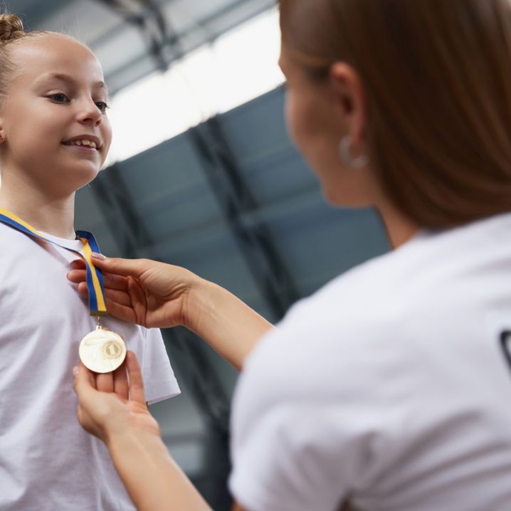 En flicka som får en medalj runt halsen av sin tränare