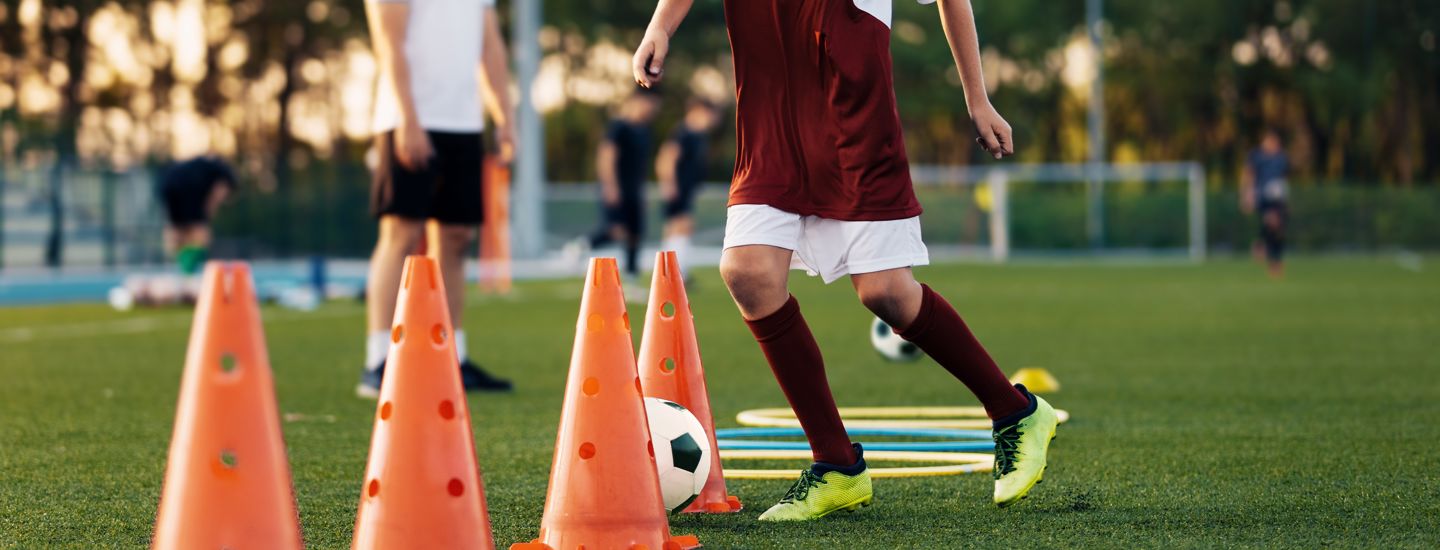 Barn som värmer upp innan träning och sparkar fotboll mellan koner