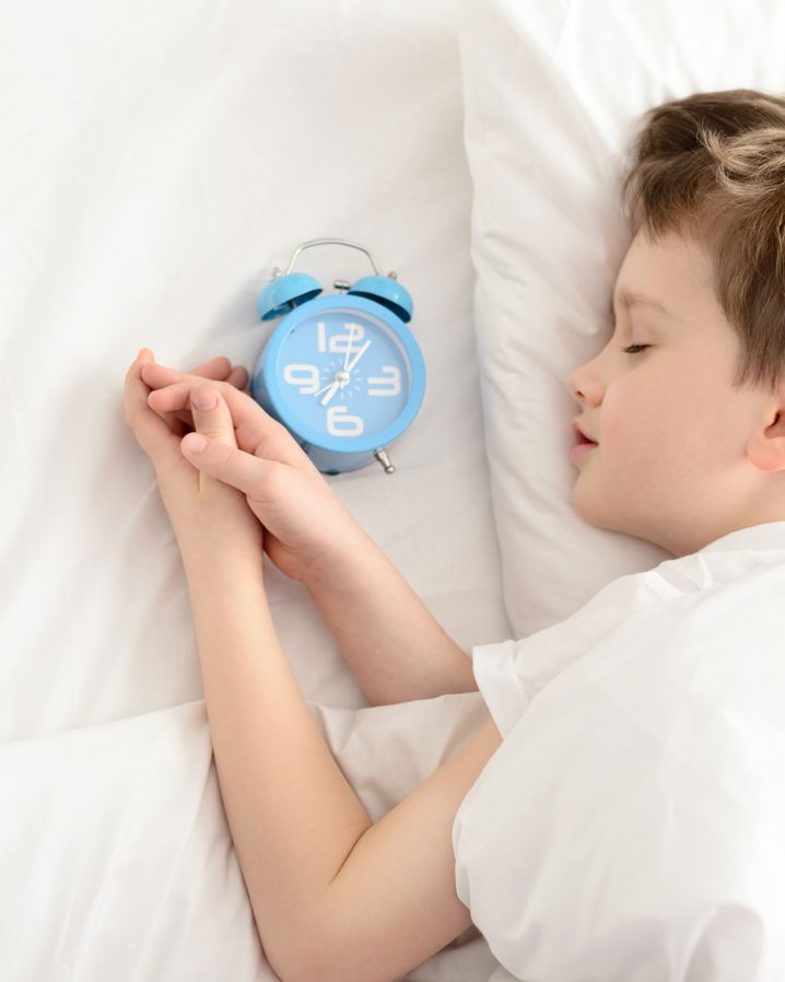 en pojke som ligger i en säng och sover med en klocka bredvid sig