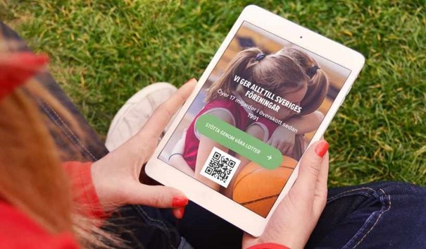 Person håller i en mobil eller surfplatta med QR-kod på skärmen, sittandes utomhus.
