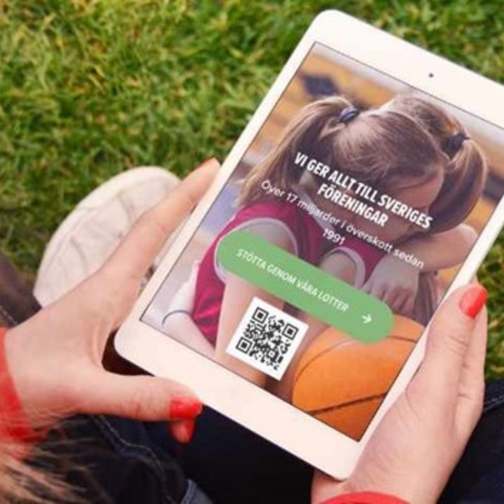 Person håller i en mobil eller surfplatta med QR-kod på skärmen, sittandes utomhus.