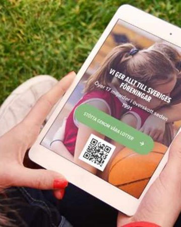 Person håller i en mobil eller surfplatta med QR-kod på skärmen, sittandes utomhus.