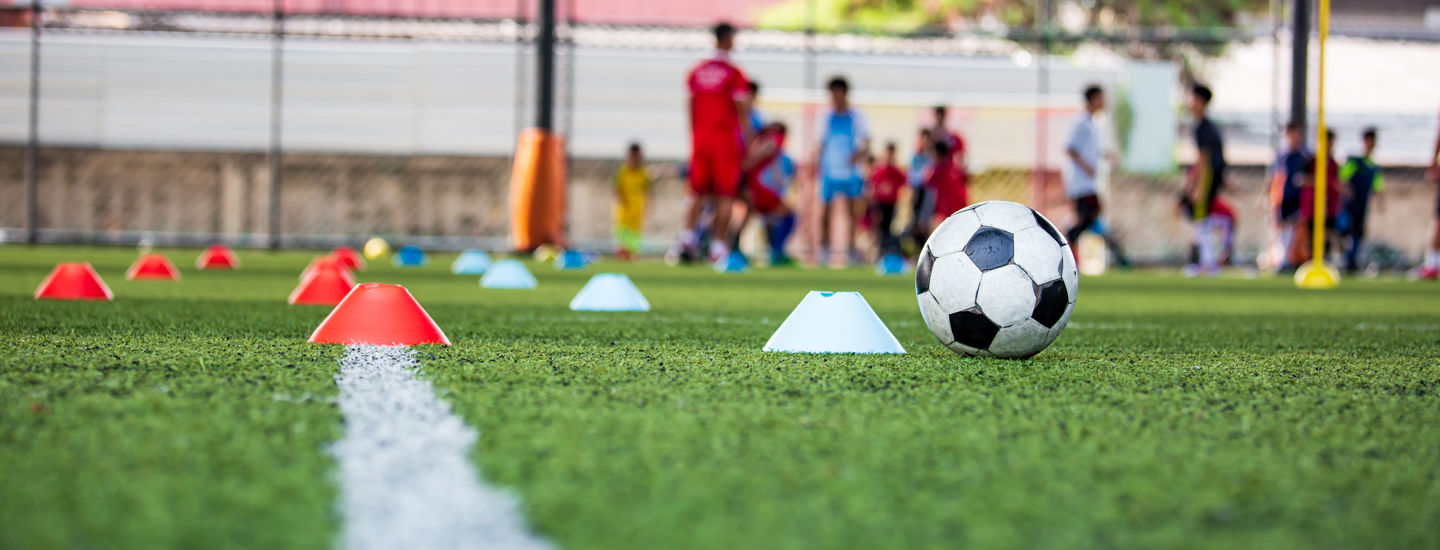 En fotbollsplan med en fotboll, utspridda konor i rött och vitt och ett fotbollslag i bakgrunden