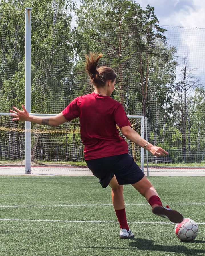 En ung tjej i fotbollskläder på en gräsplan skjuter en fotboll mot mål 