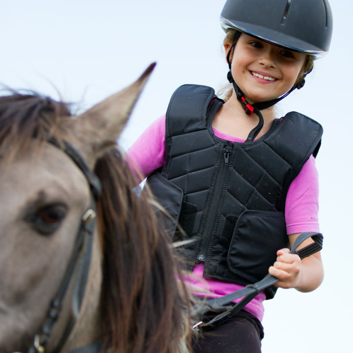 En leende flicka i ridhjälm, och ridväst rider på en häst