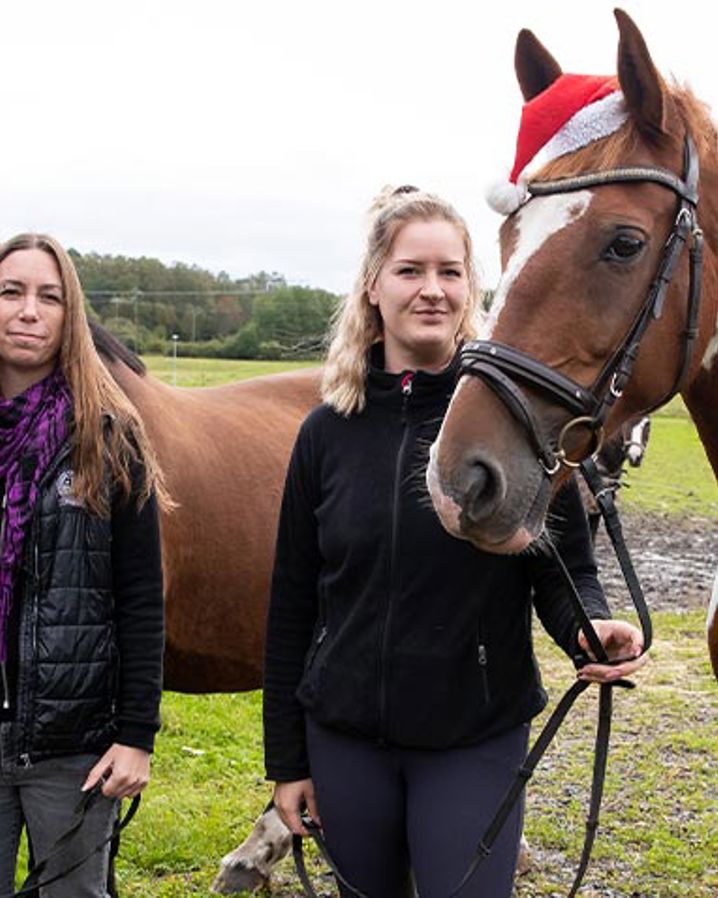 Två tjejer håller i två tränsade hästar som har tomteluvor på sig