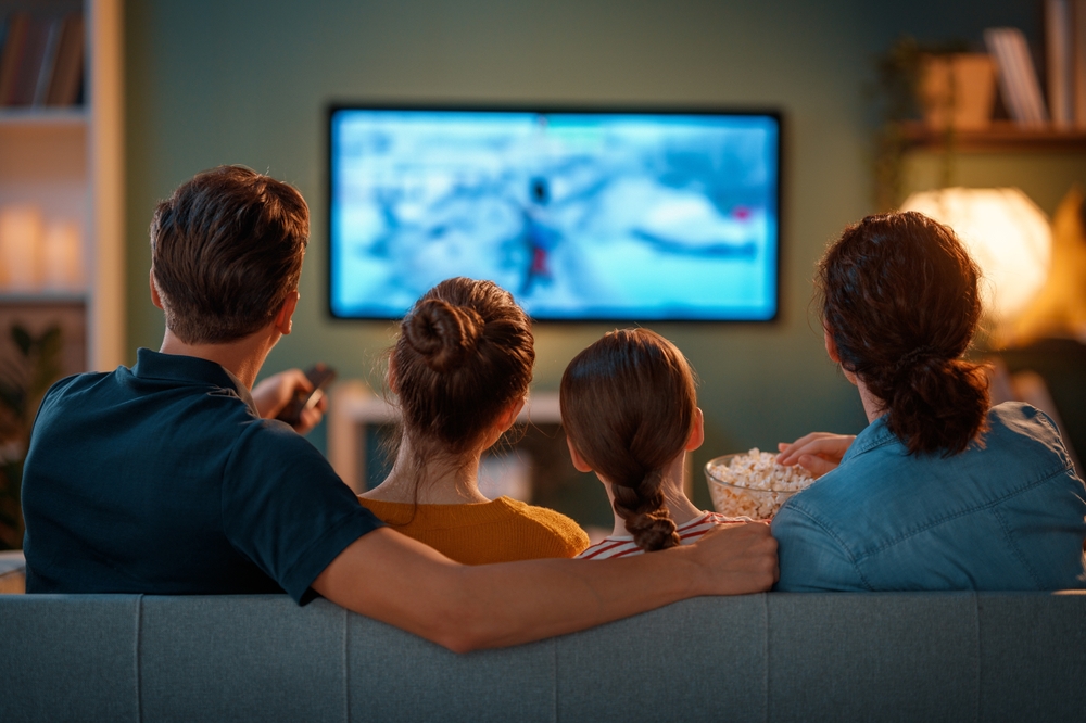 Familj spenderar tid tillsammans. Mor, far och barn tittar på TV, filmer med popcorn på kvällen hemma.