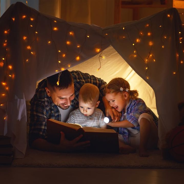 Pappa och barn läser en bok i ett tält inomhus