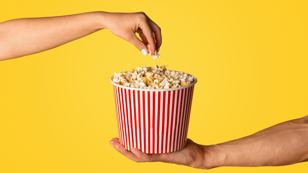 Man och kvinna med jumbo hink av popcorn på orange bakgrund, närbild av händer
