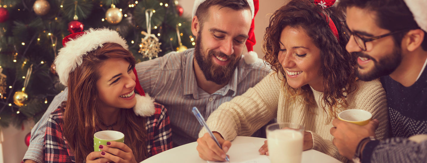 En samling vänner med tomtemössor i ett juligt inrätt rum dricker kaffe och quizar tillsammans