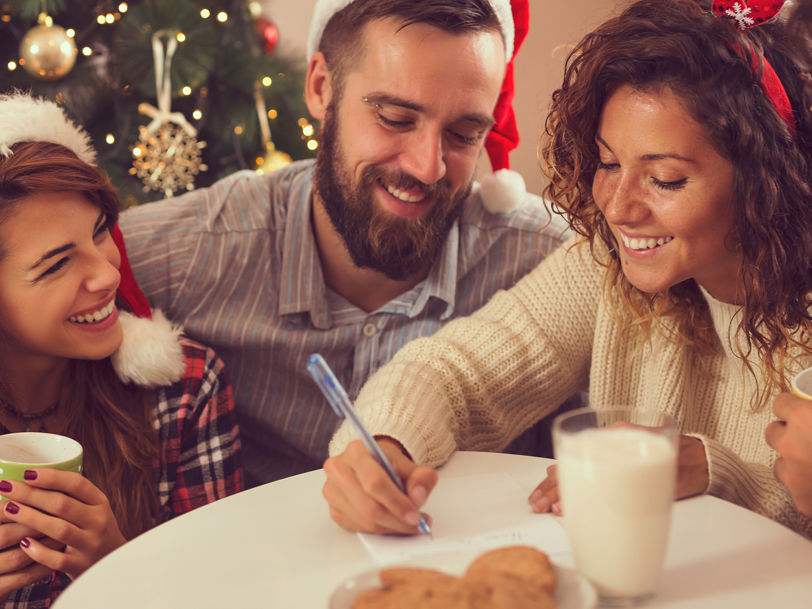 En samling vänner med tomtemössor i ett juligt inrätt rum dricker kaffe och quizar tillsammans