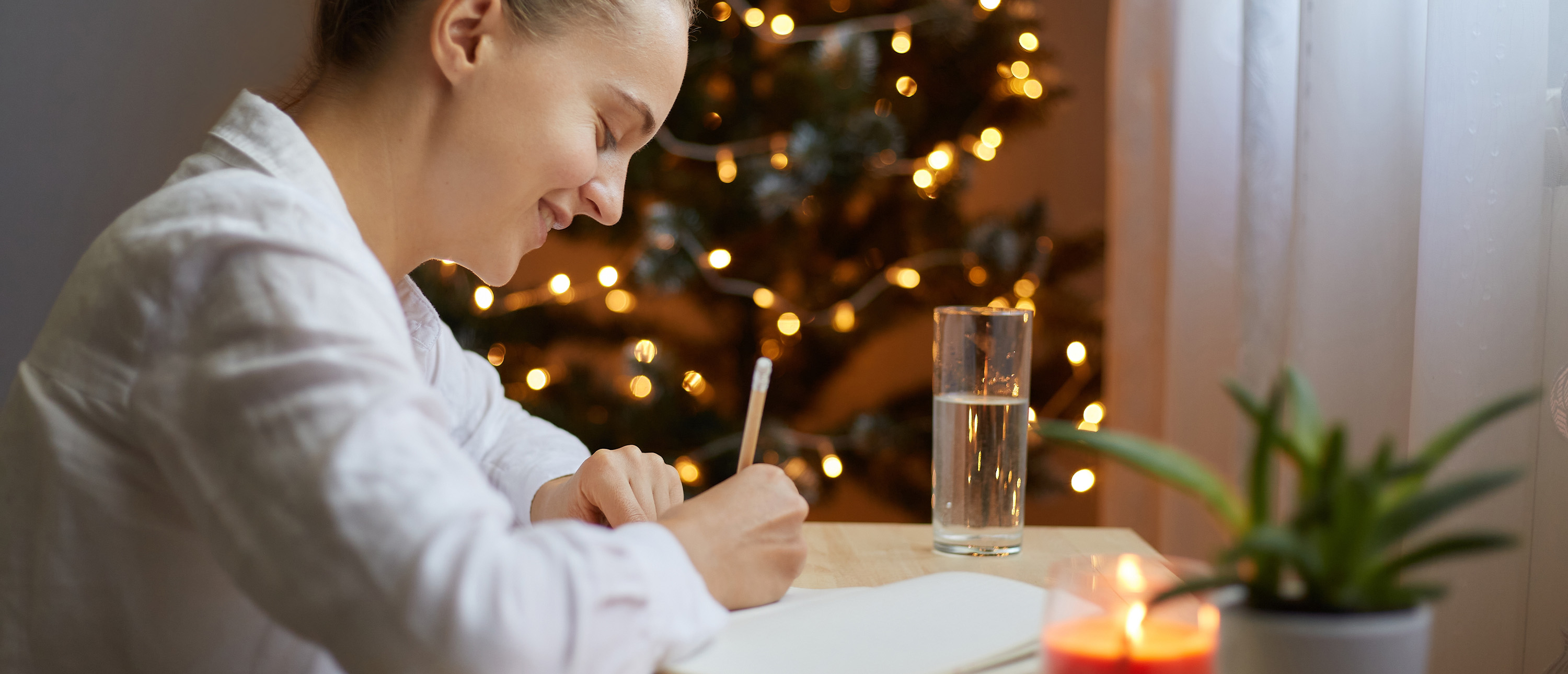 En kvinna skriver julrim i ett juligt inrett rum med tända ljus och en glimmande gran