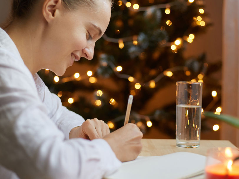 En kvinna skriver julrim i ett juligt inrett rum med tända ljus och en glimmande gran
