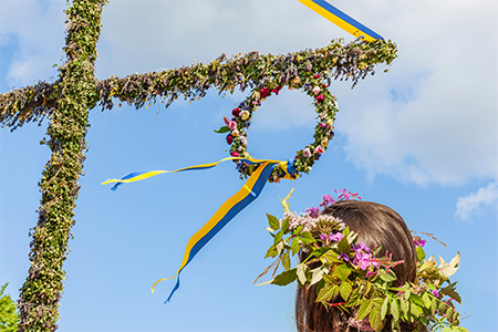 En grönklädd midsommarstång och en kvinna med en krans i håret