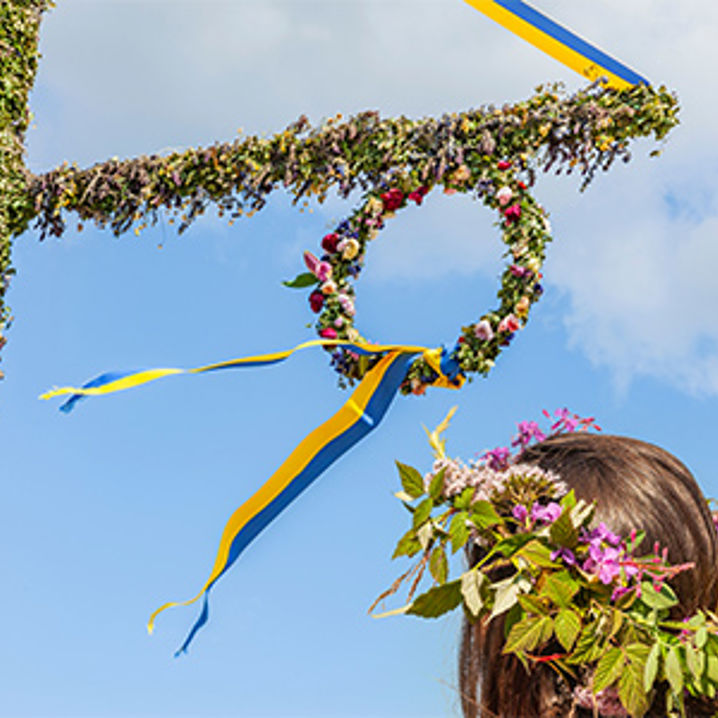 En grönklädd midsommarstång och en kvinna med en krans i håret