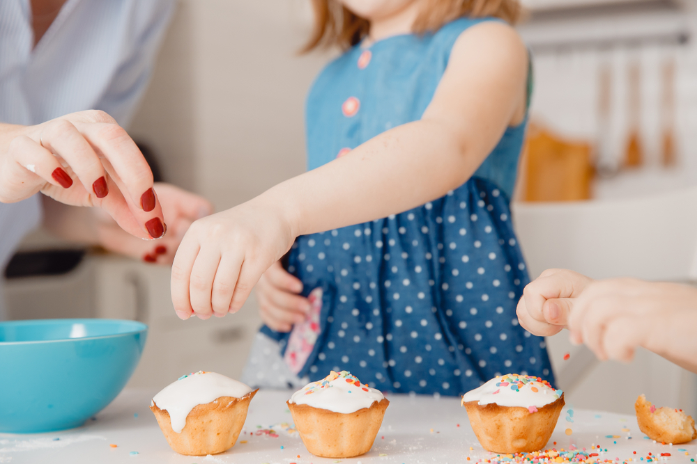 Förälder hjälper barn att strö färgade småbitar över muffins med sina händer