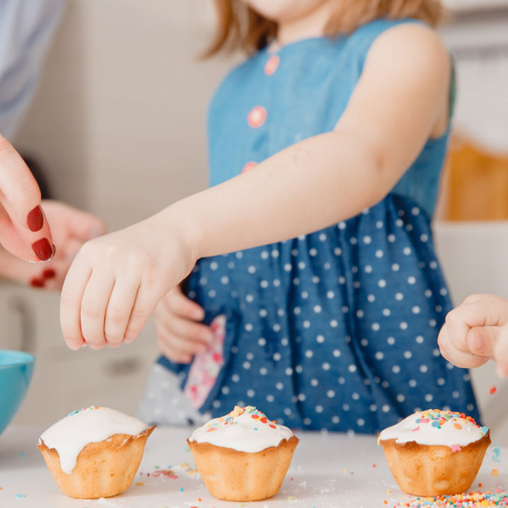 Förälder hjälper barn att strö färgade småbitar över muffins med sina händer