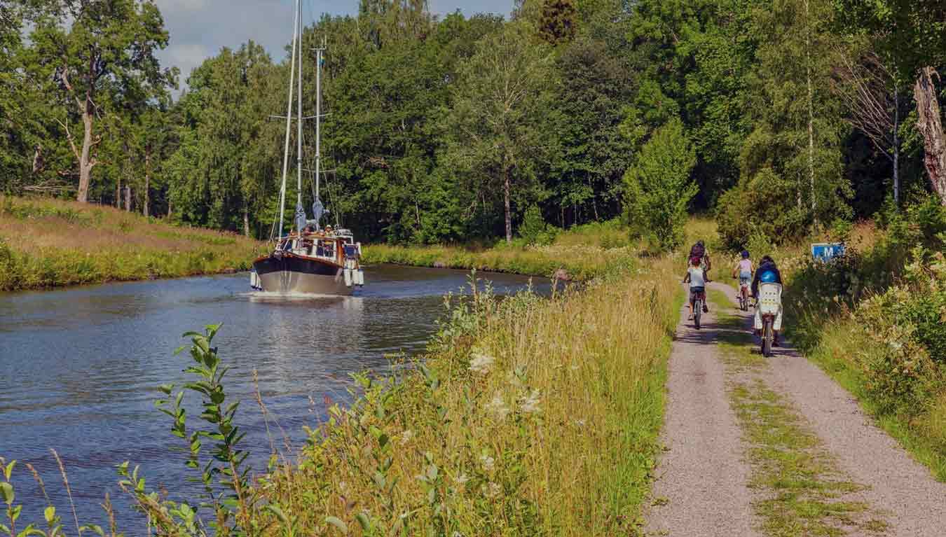 Cyklister och en båt i en kanal i ett idylliskt landskap