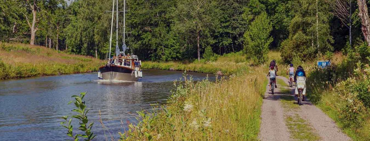 Cyklister och en båt i en kanal i ett idylliskt landskap