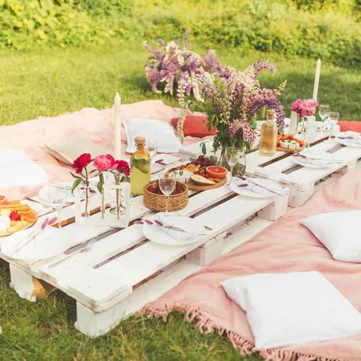 Ett somrigt dukat bord i trädgården med kuddar och filtar på marken