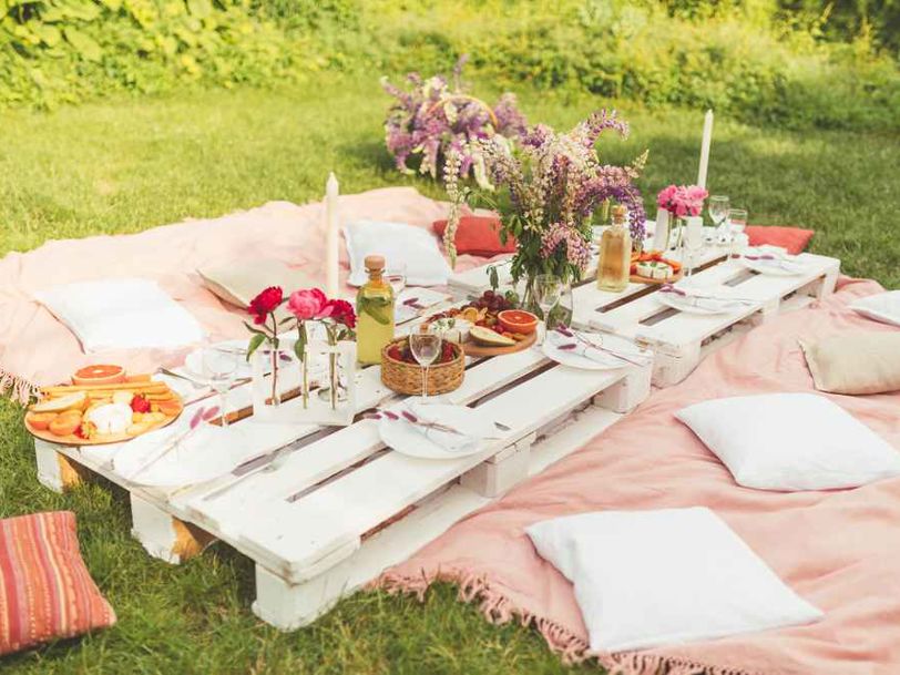 Ett somrigt dukat bord i trädgården med kuddar och filtar på marken