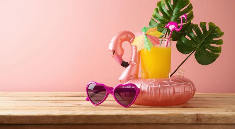 På träbord ligger solglasögon, en paraplydrink, en växt och en uppblåsbar flamengo