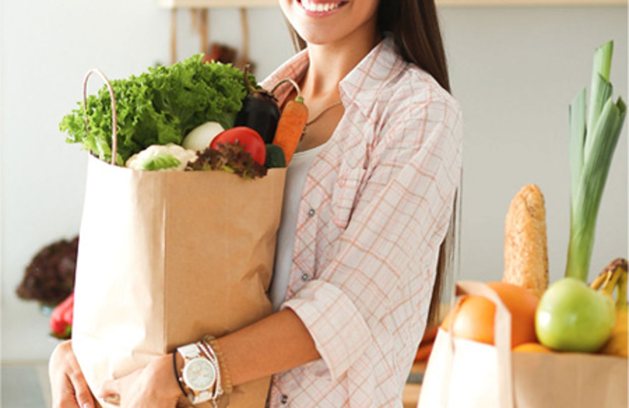 Kvinna med en grönsaksfylld matkasse i famnen