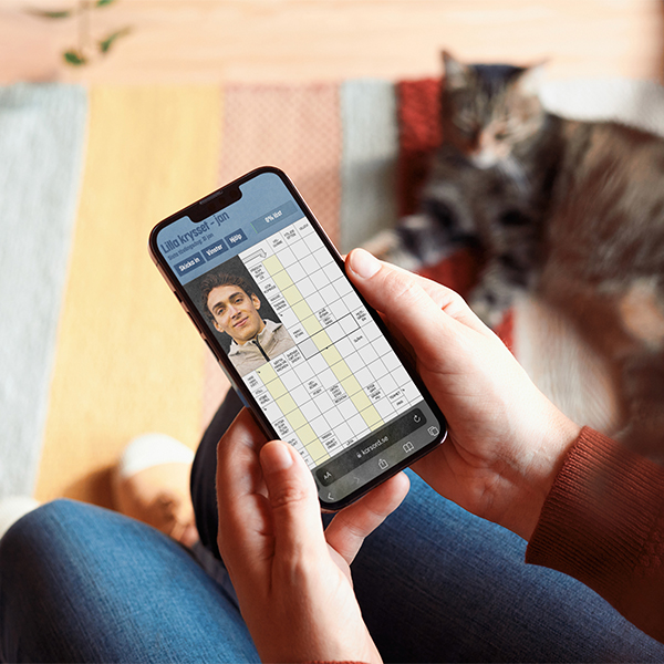 Person löser digitalt korsord på mobil med en katt vilande i bakgrunden.