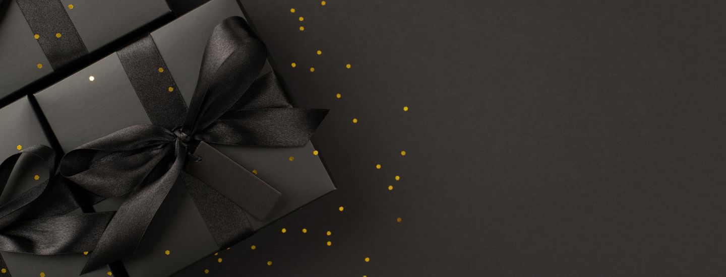 Svarta paket med svart sidensnöre liggandes på en svart bakgrund, allt med guldglitter ovanpå