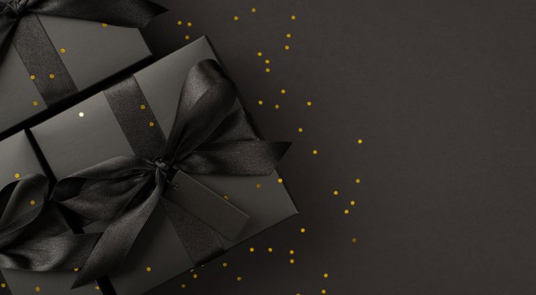 Svarta paket med svart sidensnöre liggandes på en svart bakgrund, allt med guldglitter ovanpå