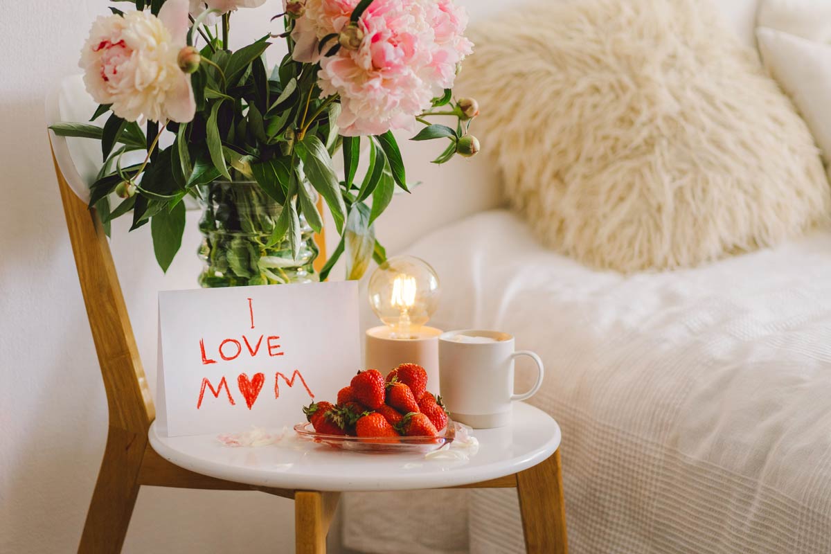 Nattduksbord dukat med kaffe, jordgubbar, pioner i vas och en teckning som säger "I love mom"