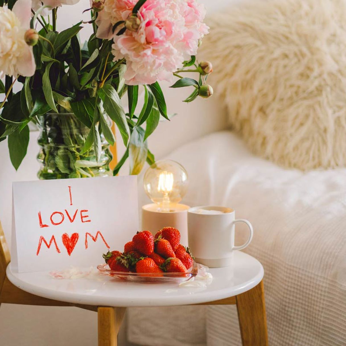 Nattduksbord dukat med kaffe, jordgubbar, pioner i vas och en teckning som säger "I love mom"