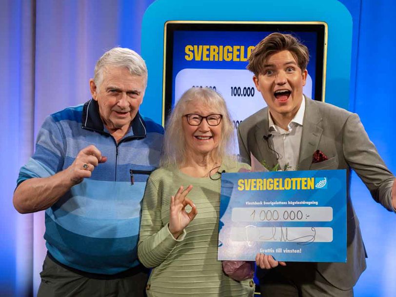Två vinnare med Sverigelotten-check tillsammans med programledare.